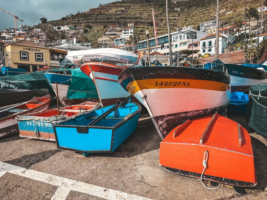 Close-up of several colourful wooden fishing boats (blue, orange, white with a yellow stripe) with registration numbers, with the Anonimo building behind.