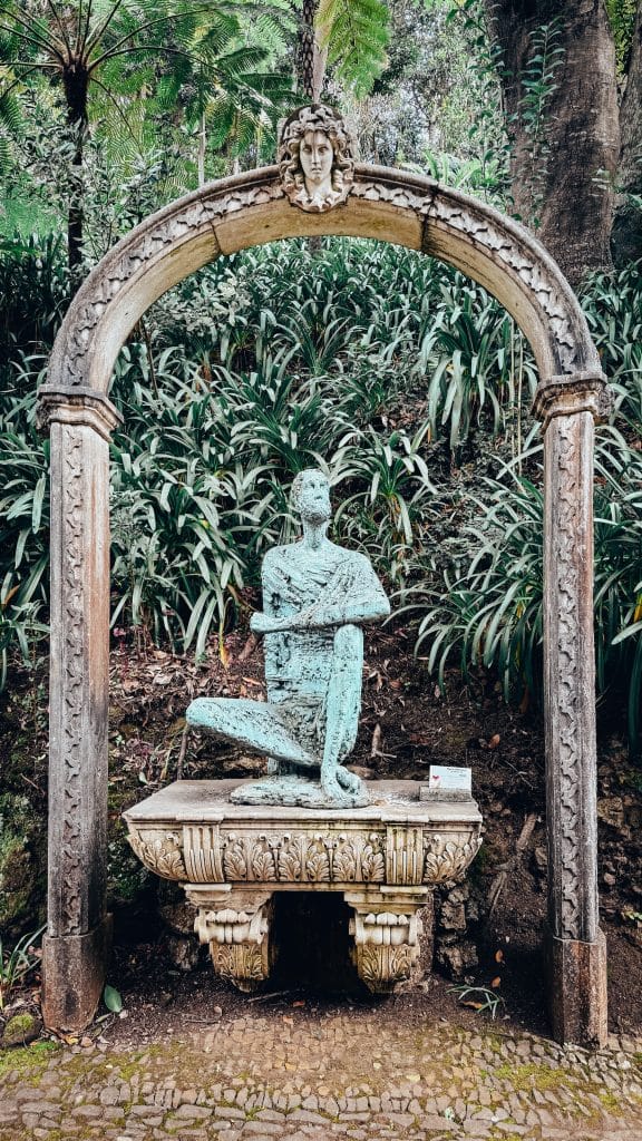 A patinated bronze sculpture under a stone arch amid lush tropical plants at Monte Palace. Photo: Ewelina Podrez-Siama 2025