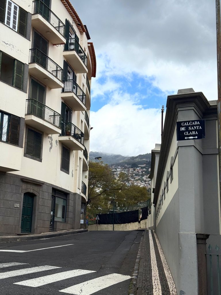 Street name sign for Calçada de Santa Clara on the corner of a building next to a pedestrian crossing