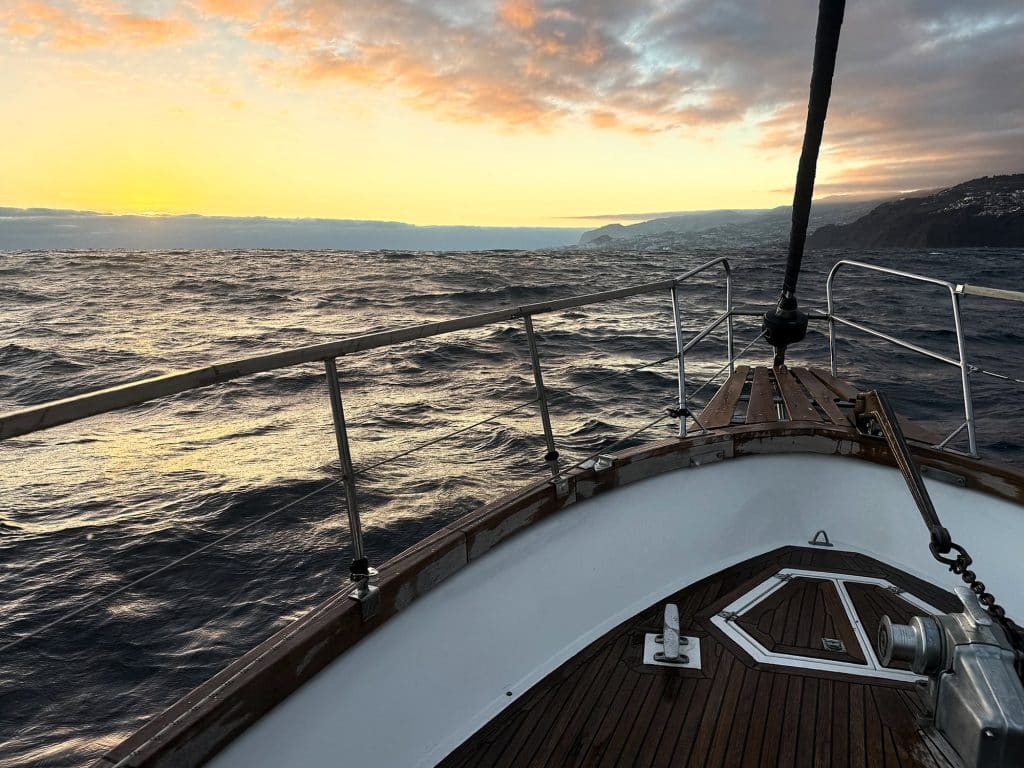 Wooden deck and bow of a yacht on a choppy ocean at sunset