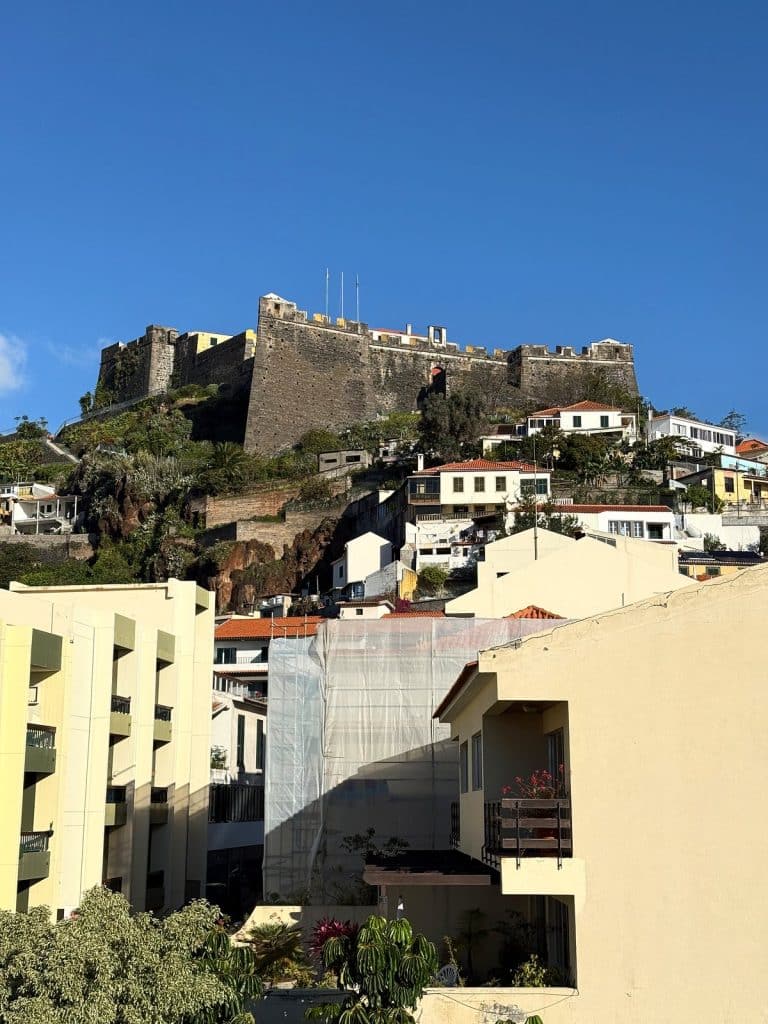 The stone walls of Fortaleza do Pico with flags on the hill, white houses and pale apartment blocks of central Funchal below