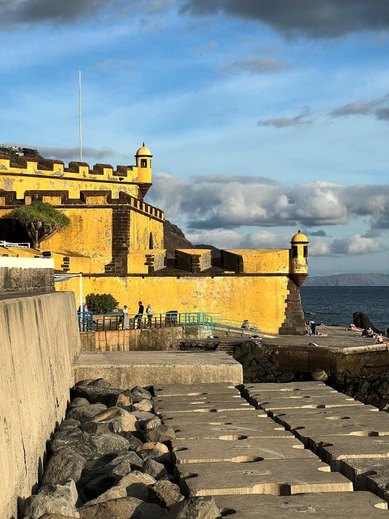 The yellow battlemented walls of the fort with a corner watchtower topped by a small dome, clouds and the ocean behind