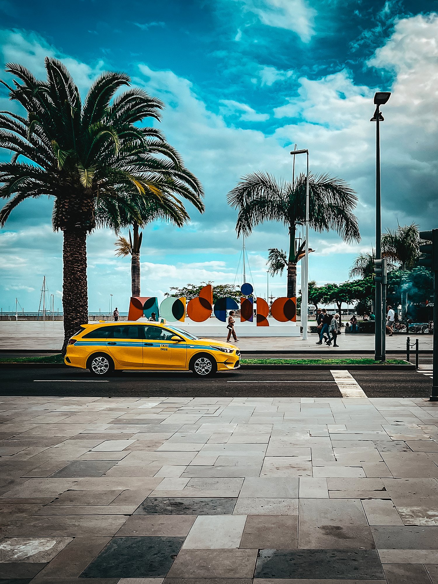 Yellow taxi on Avenida do Mar in Funchal, with palms and the colourful Madeira sign behind