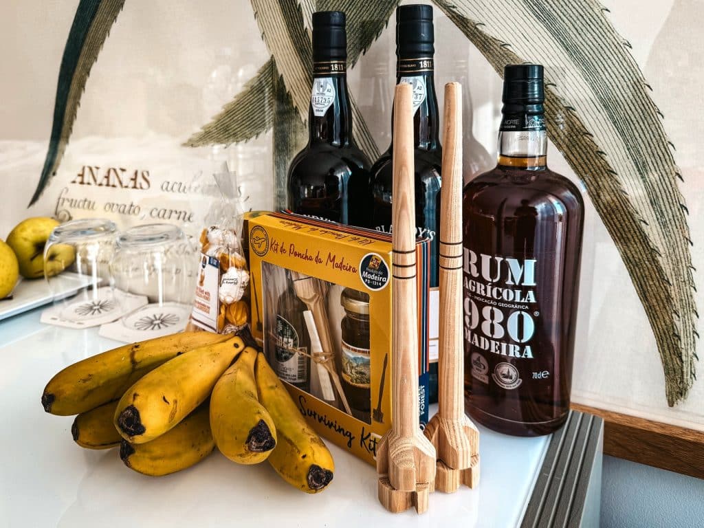 Bottles of Madeira wine and rum, bananas, sweets and wooden poncha stirrers on a table in a hotel room