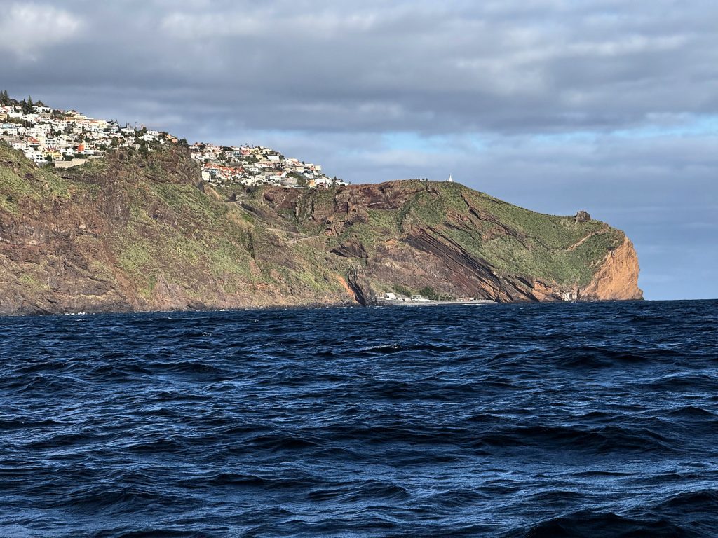 Red and green cliffs with buildings on top, seen from a yacht east of Funchal