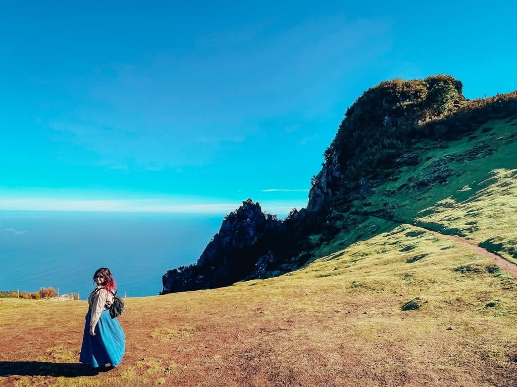 A woman walking along a path on the plateau, with the ocean and tall rocks in the background