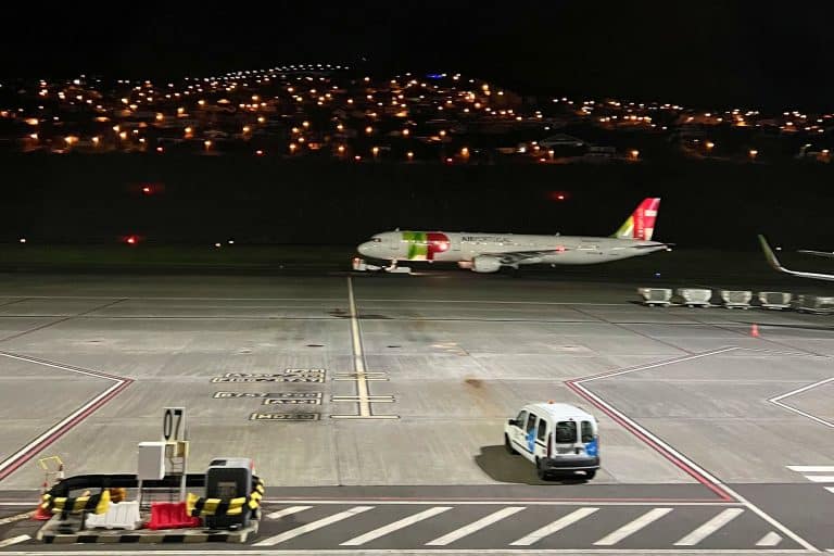 A TAP plane on the apron at Madeira Airport at night, with house lights on the hillside behind