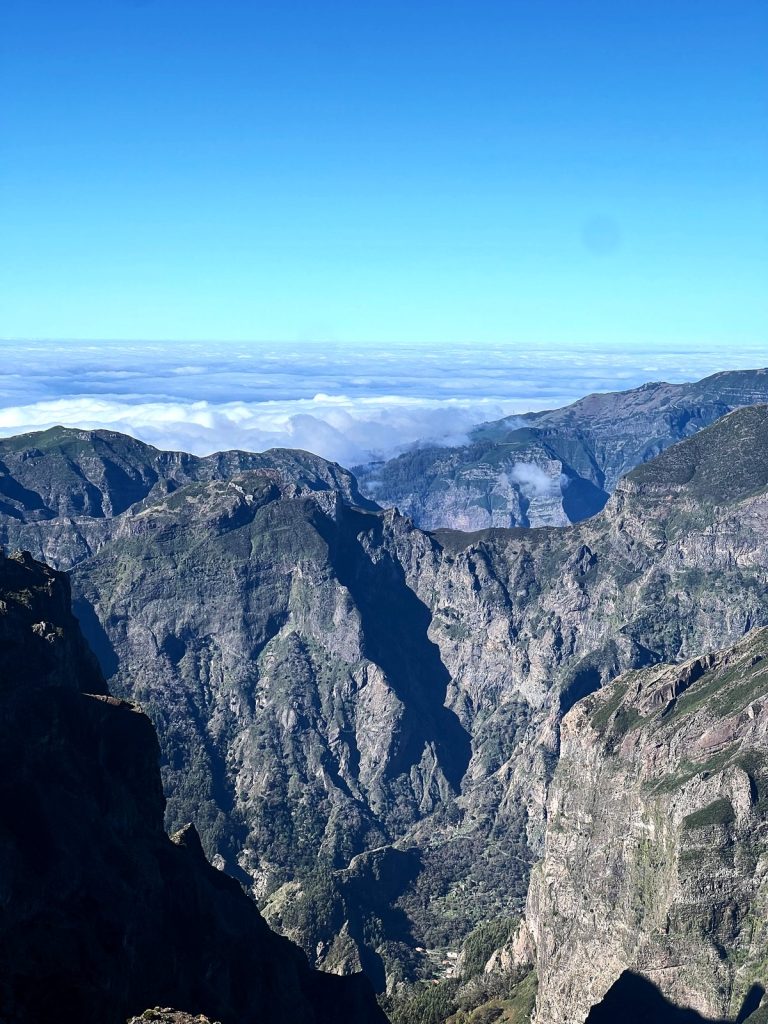 Steep, jagged valleys and ridges in the centre of Madeira, with a sea of clouds and blue sky above