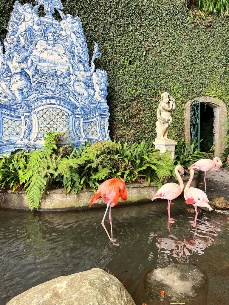 Pink flamingos in a pond in front of a blue-and-white azulejo panel and a white statue in the Monte Palace garden