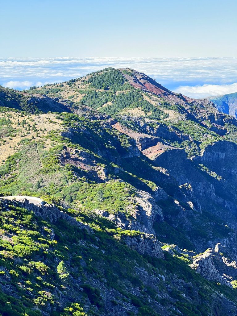 Green and brown mountain ridges in the centre of Madeira in the sun, with clouds on the horizon
