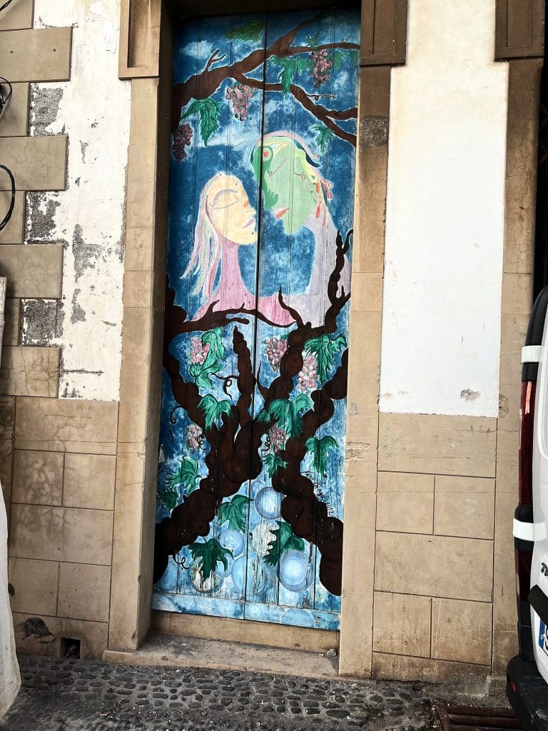 A door painted with a tree and two figures on a blue background, in the stone frame of an old town house