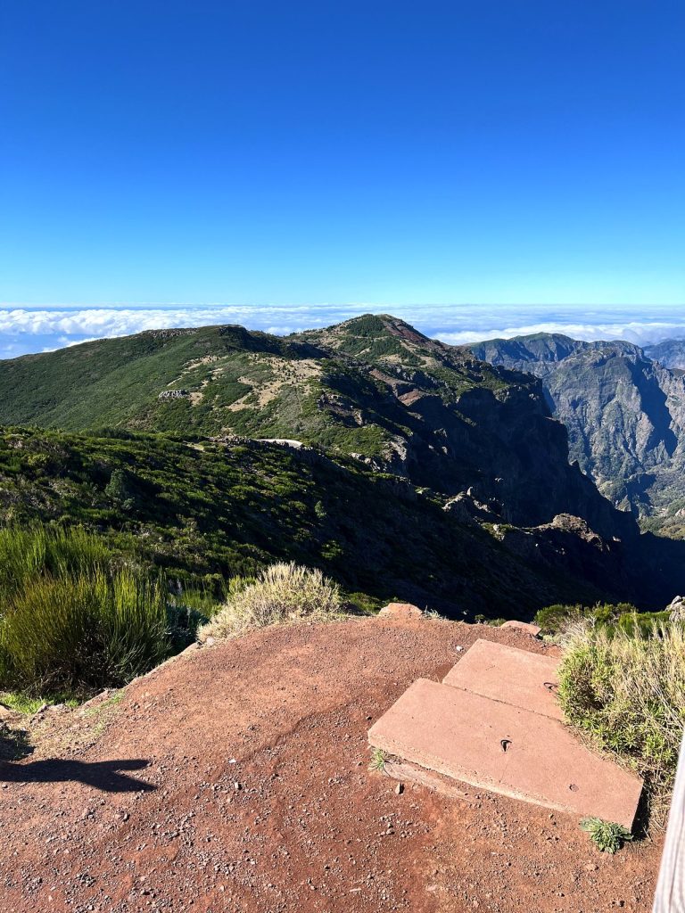 A red path and concrete slabs at a viewpoint, with green mountain ridges and a sea of clouds beyond