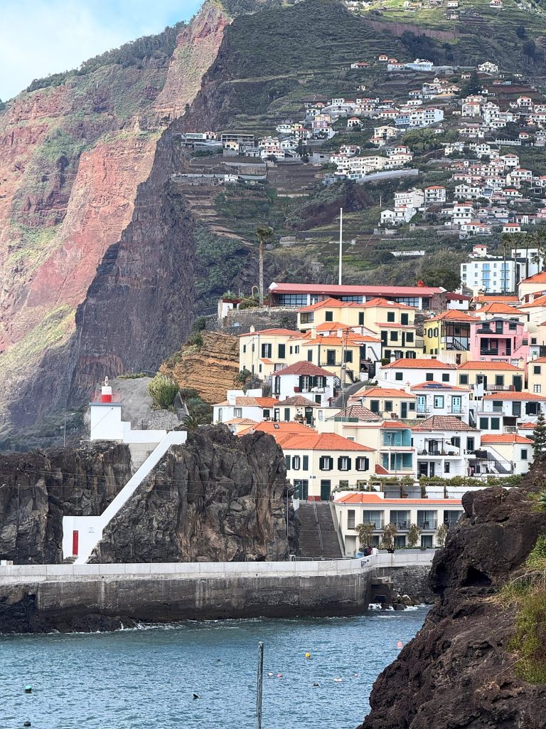Colourful houses of Câmara de Lobos on a rock above the water, with the red cliff face and terraces on the hillside behind