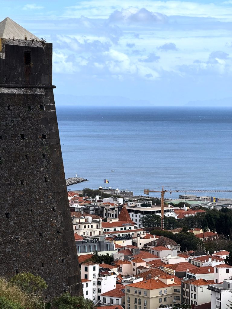 The dark stone tower of the Fortaleza do Pico above the rooftops of central Funchal and the ocean