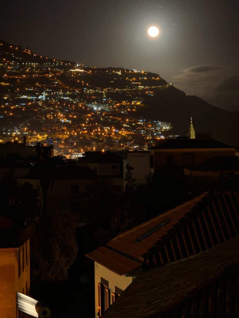A full moon over Funchal’s hillside full of lights, with dark rooftops in the foreground