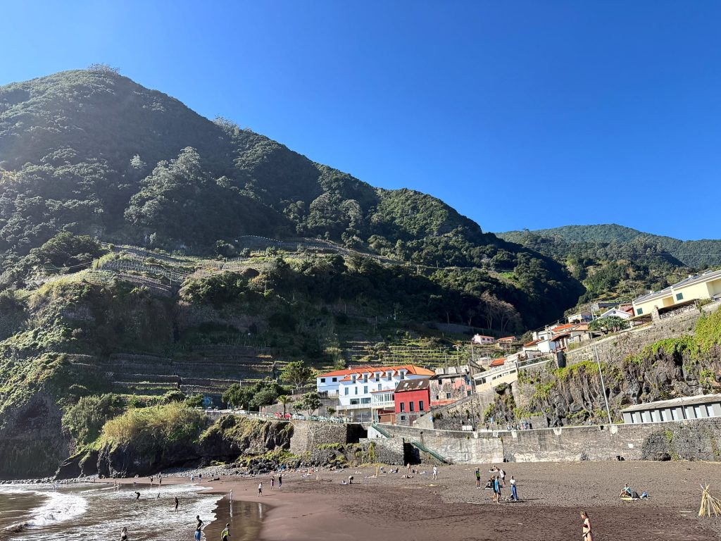 The black sand beach at Seixal below a green mountain on a sunny February day