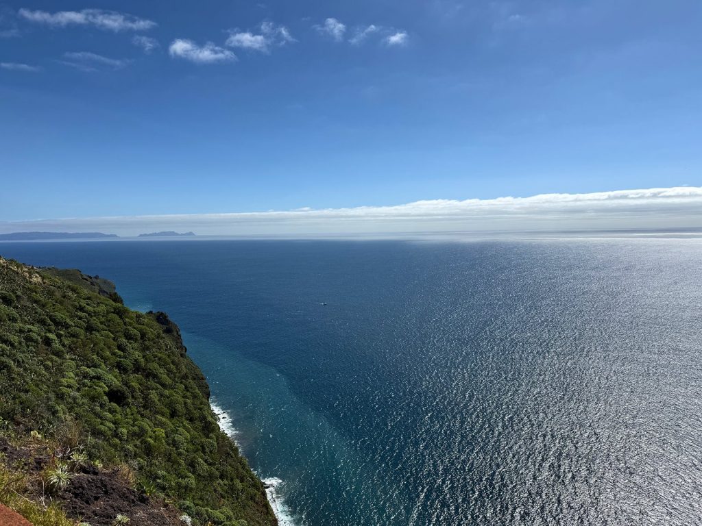 A green cliff slope dropping into the ocean, a band of cloud on the horizon
