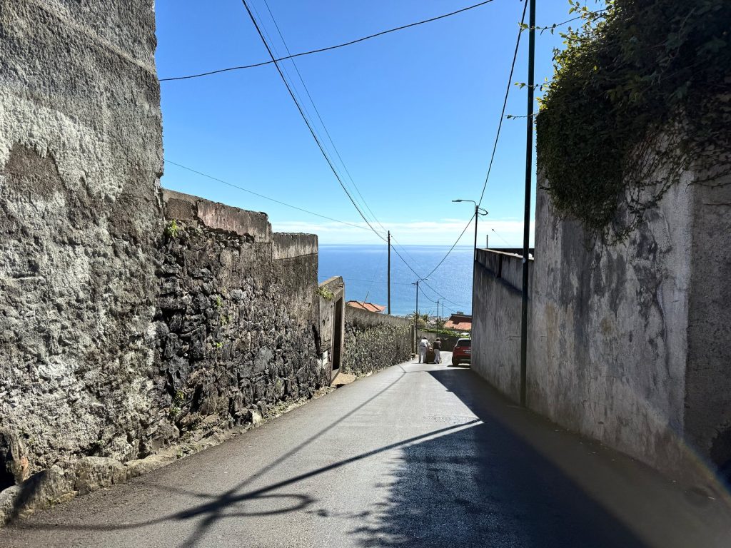 A narrow, steep street between high stone walls with a view of the ocean at the end