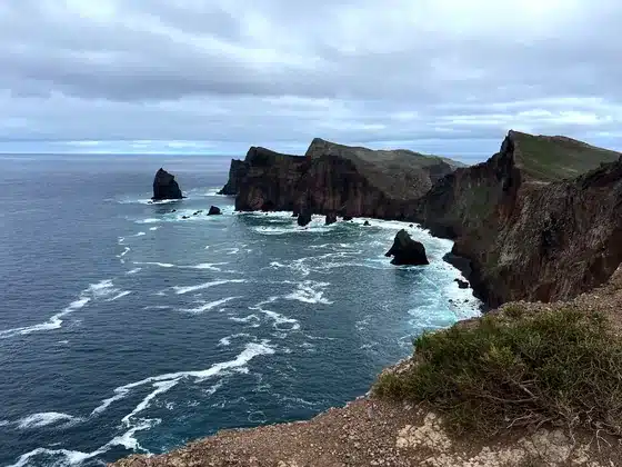 The cliffs of Ponta de São Lourenço dropping into a bay, rock spires in the foaming ocean