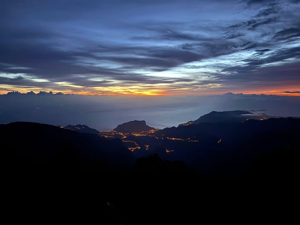Village lights in the valley and an orange horizon before sunrise on Pico do Arieiro
