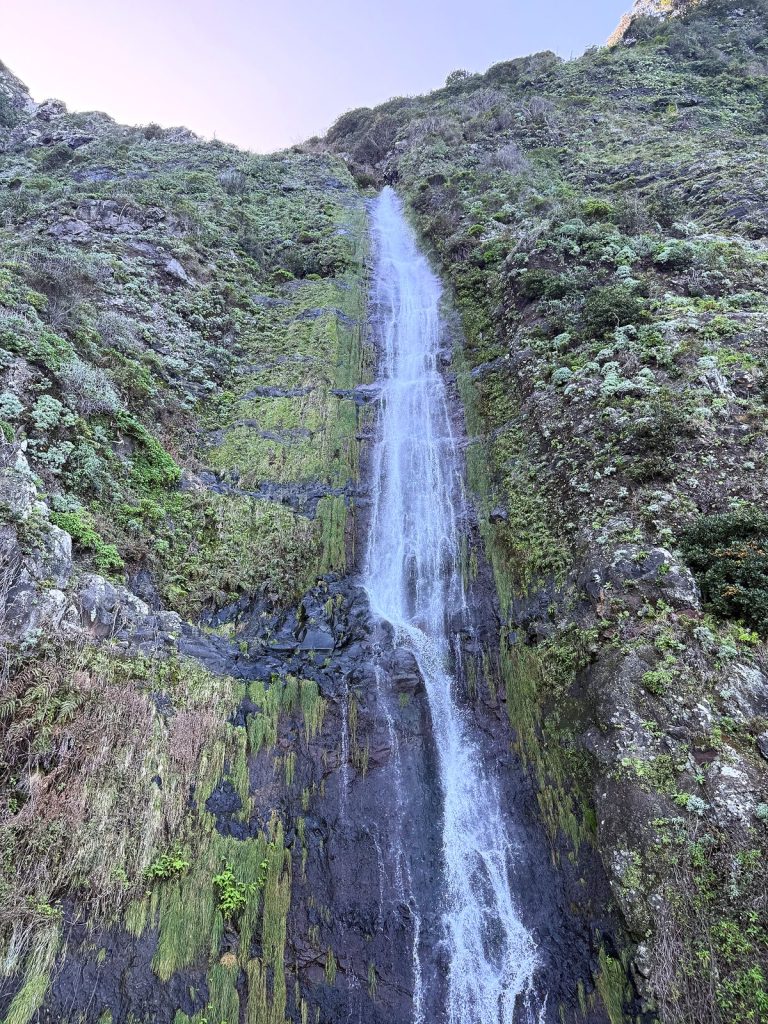 A waterfall falling in a wide cascade down a moss-covered rock wall