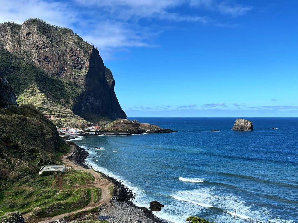 A pebbly beach and waves on the Porto da Cruz coast, with Penha d’Águia behind