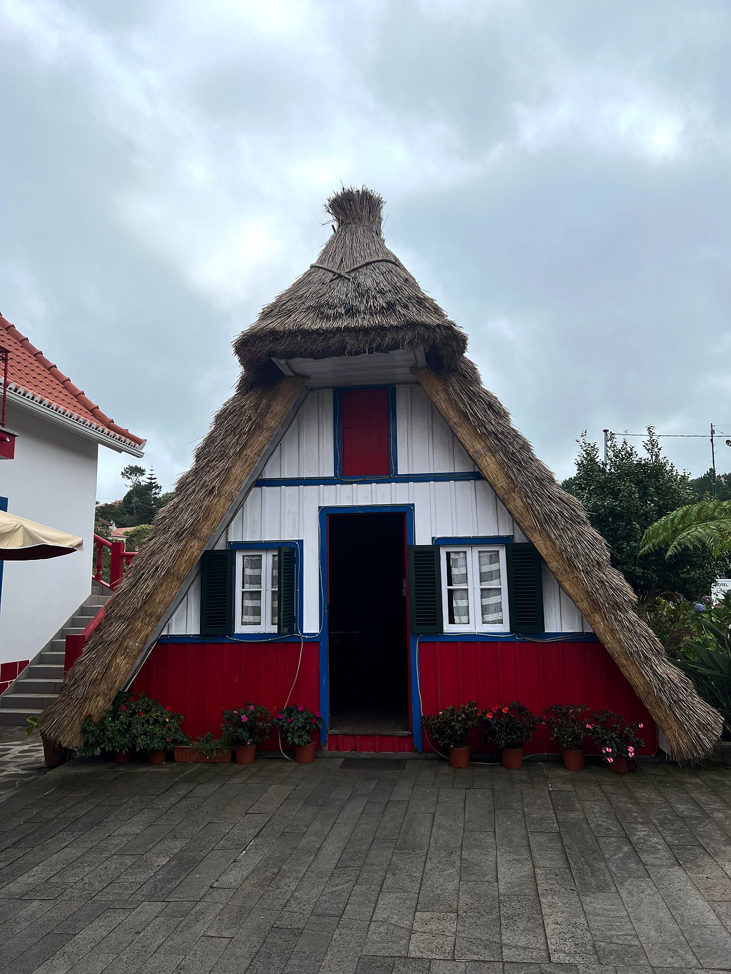 Triangular thatched house in Santana, white and red with blue trim, flower pots by the door