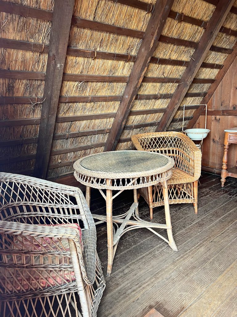 A wicker table and armchairs under the sloping thatched roof inside a house