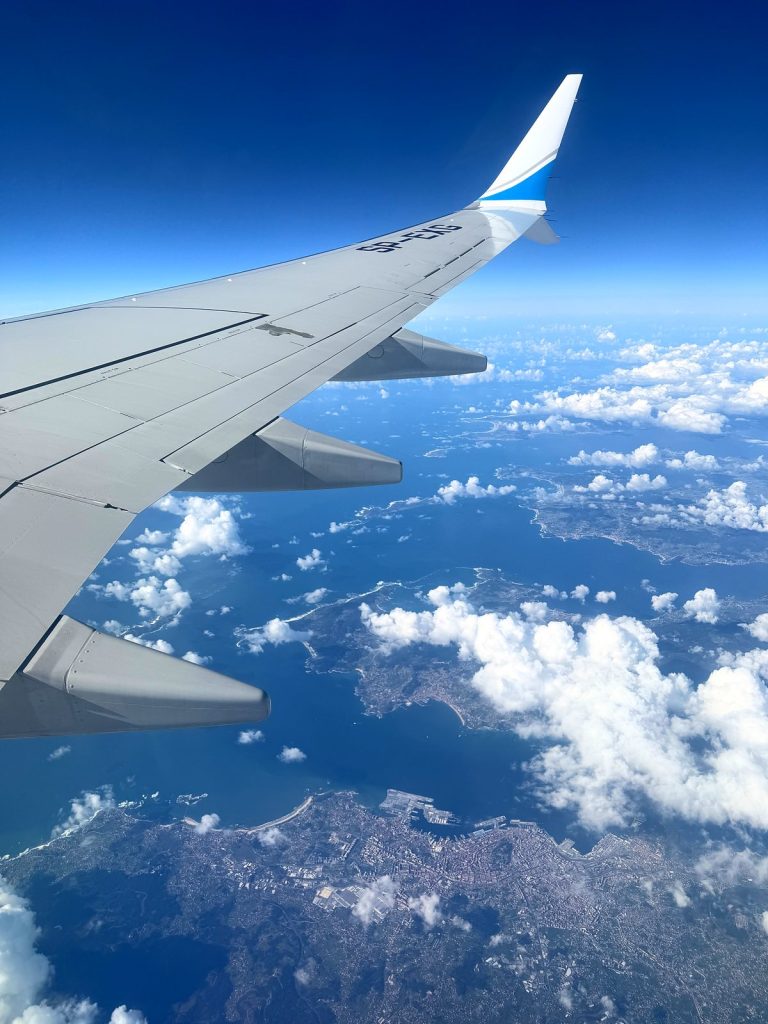 An aircraft wing above the clouds and the coastline, seen from the window